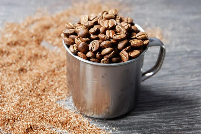 Stainless steel cup filled with coffee beans next to coffee powder