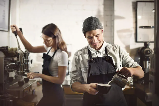 Two baristas making coffees in café