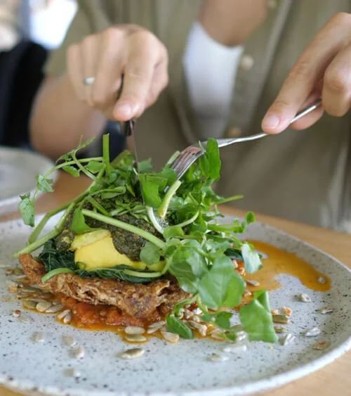 Customer cutting vegan sandwich with cutlery at café table