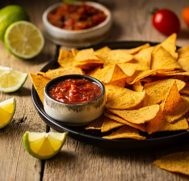 Single big black plate of yellow corn tortilla nachos chips with salsa sauce over wooden table