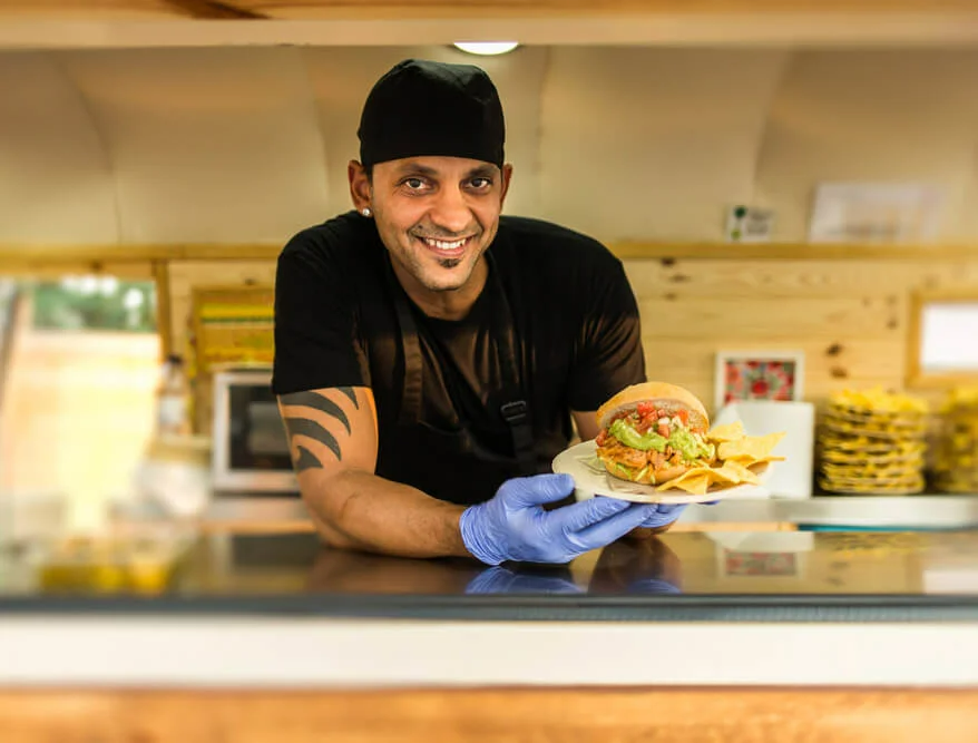 Smiling chef in uniform looking at camera while holding plate with served burger