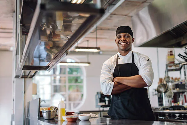 Happy chef with arms crossed in open restaurant kitchen