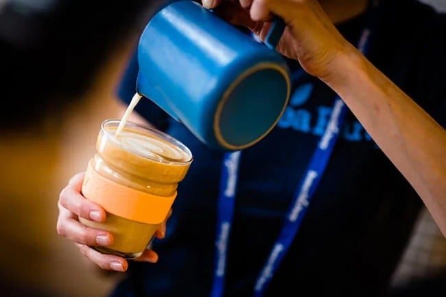 Barista pouring milk into reusable coffee cup
