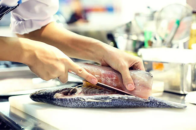 Chef gutting and filleting fish on cutting board in kitchen