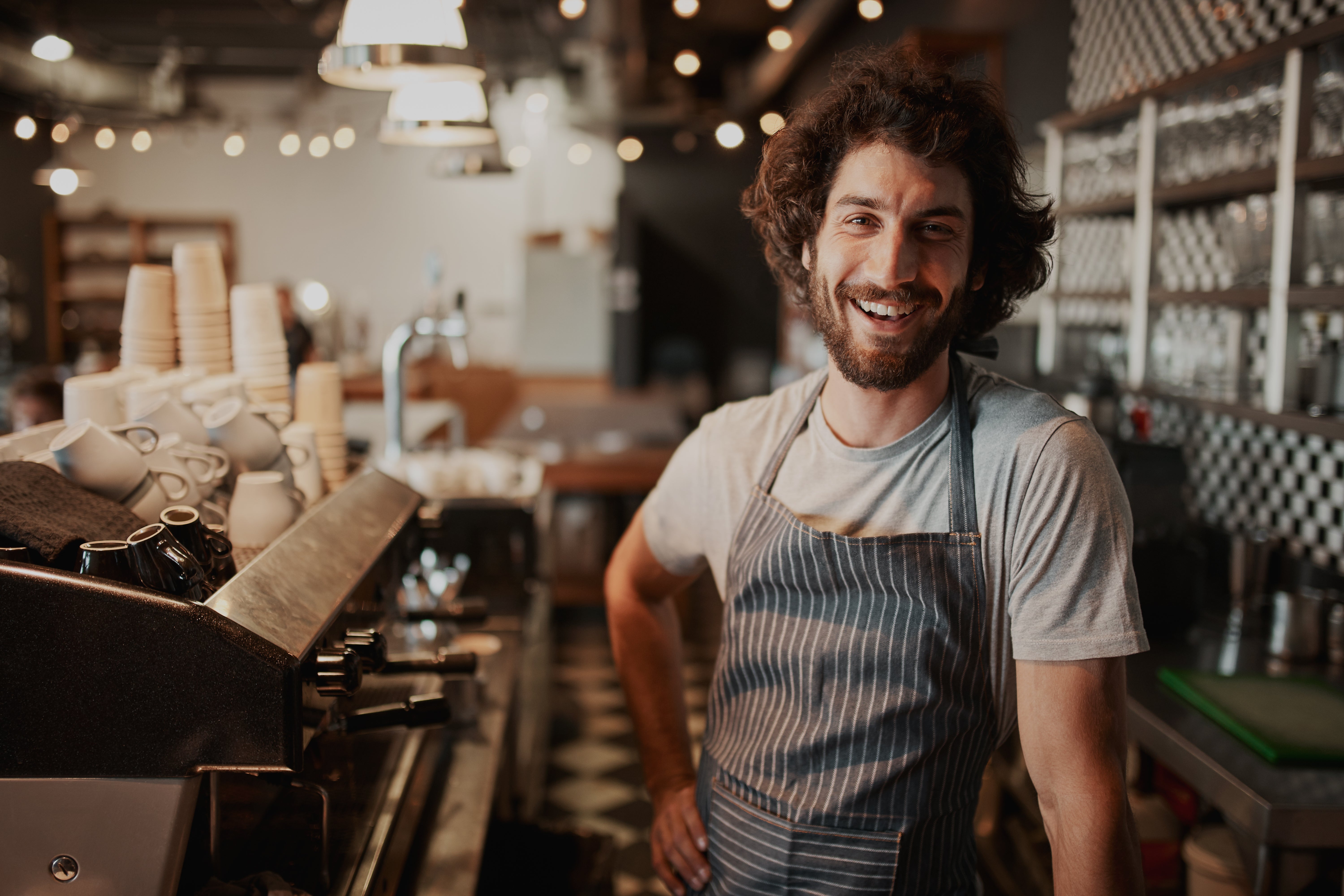 man with curly hair smiling at a coffee machine