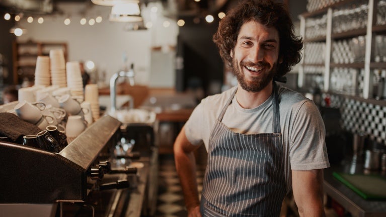man with curly hair smiling at a coffee machine