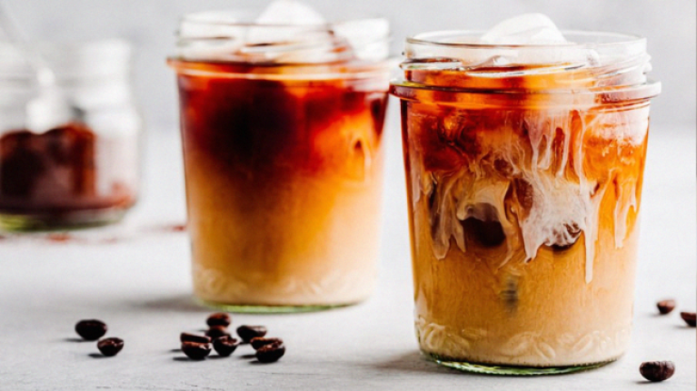 Two glasses of cold brew coffee with coffee beans scattered around them