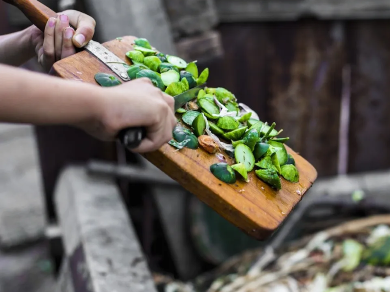 Green food scraps being scraped off cutting board into compost bin