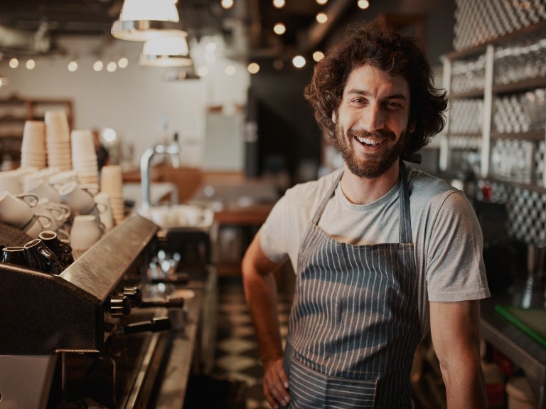 man with curly hair smiling at a coffee machine